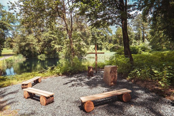 paxnatura Naturbestattung - Waldfriedhof Wundschuher See bietet einen Andachtsplatz mit einem malerischen Teich im Hintergrund